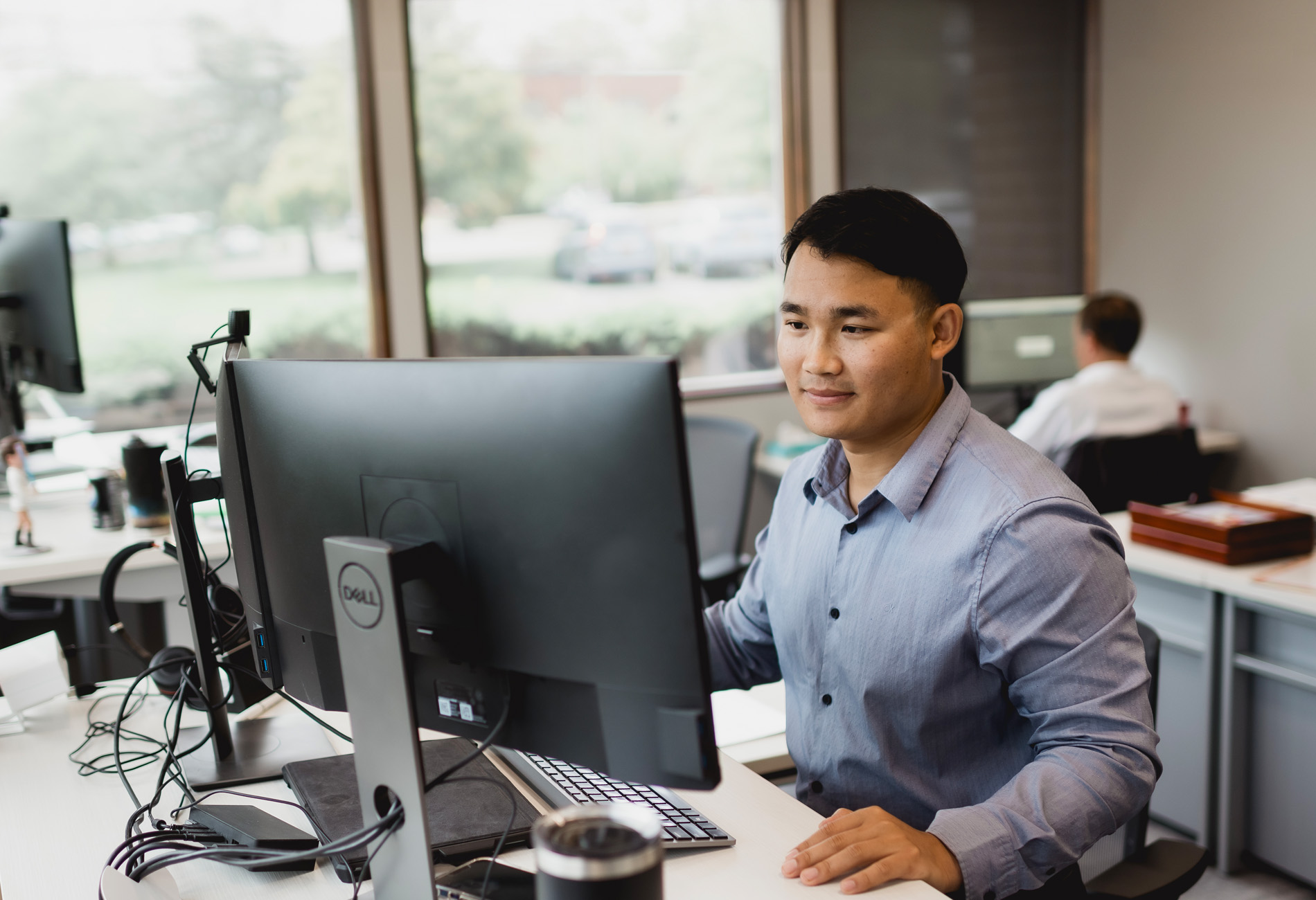 Eh Ka Paw, Investment Portfolio Administrator: a man with short black hair and a gray button down shirt working at his computer. company website bio photo.