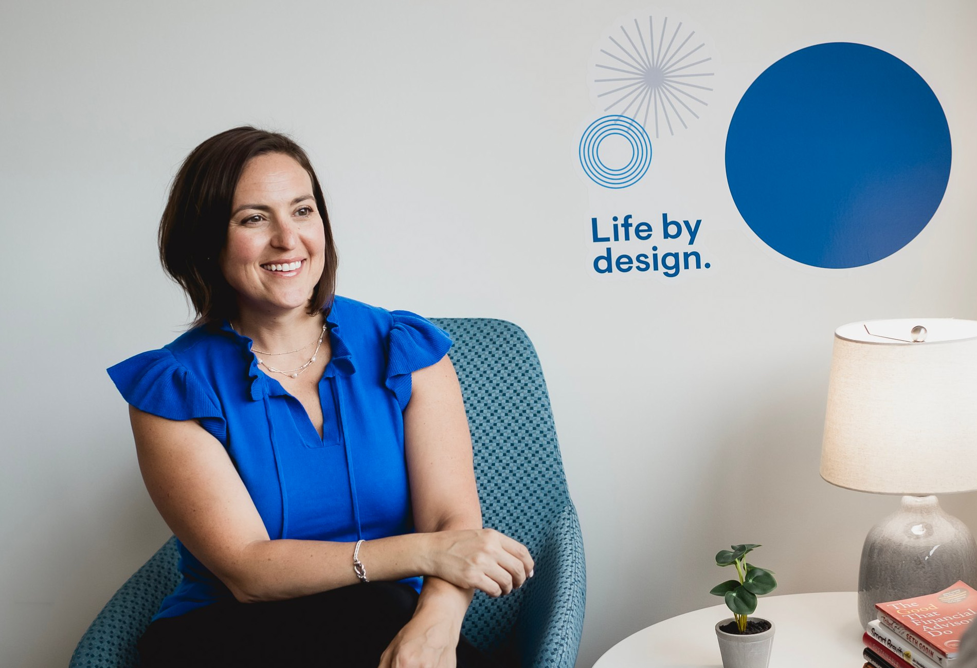 Katy Heintz, Business Development Manager, Wealth Management Leadership Team, Strategic Management Team: A woman with short brown hair wearing a blue shirt sitting in a blue chair against a white wall.